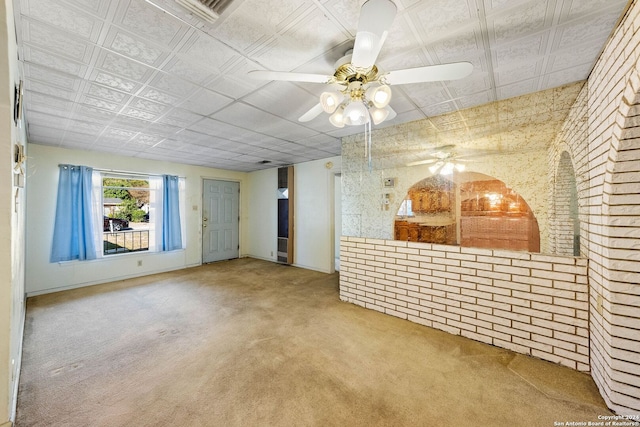 carpeted empty room featuring ceiling fan and brick wall