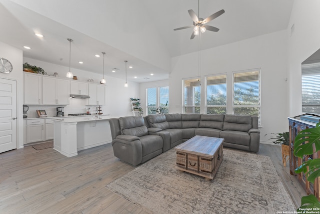 living room with ceiling fan, plenty of natural light, high vaulted ceiling, and light wood-type flooring