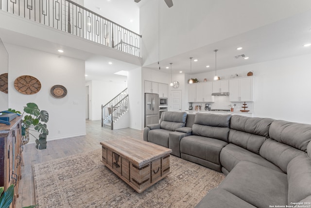 living room featuring ceiling fan, light hardwood / wood-style floors, and a towering ceiling