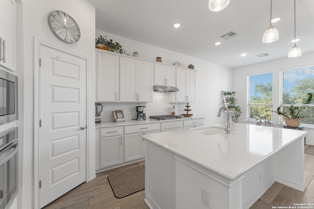 kitchen with white cabinets, a center island with sink, light hardwood / wood-style flooring, and stainless steel appliances