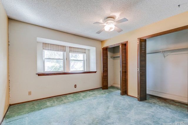 unfurnished bedroom with light carpet, a textured ceiling, two closets, and ceiling fan