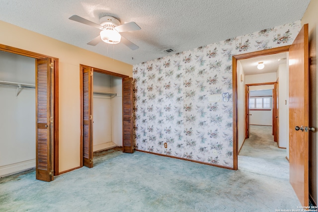 unfurnished bedroom with ceiling fan, light colored carpet, a textured ceiling, and multiple closets