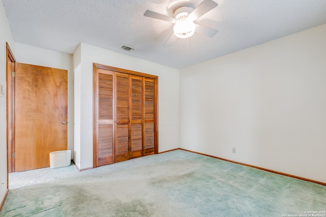 unfurnished bedroom featuring ceiling fan, a closet, light colored carpet, and a textured ceiling