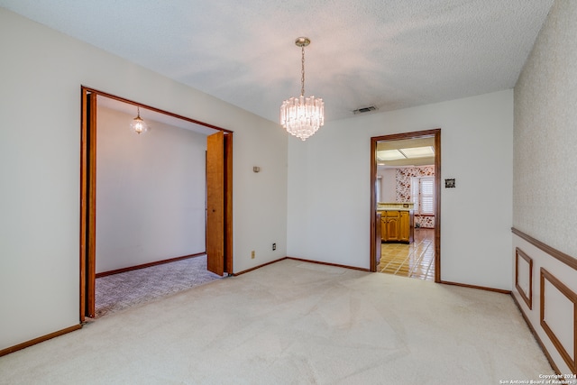 carpeted spare room with a textured ceiling and an inviting chandelier