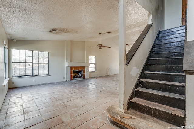 stairs with ceiling fan, a fireplace, a textured ceiling, and vaulted ceiling