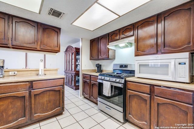 kitchen featuring dark brown cabinets, light tile patterned flooring, a textured ceiling, and gas range