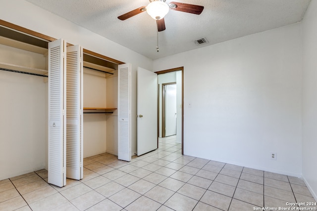 unfurnished bedroom featuring ceiling fan, light tile patterned flooring, a textured ceiling, and two closets