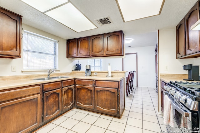 kitchen featuring sink, kitchen peninsula, a textured ceiling, light tile patterned flooring, and stainless steel range with gas stovetop