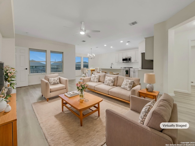 living room with light hardwood / wood-style floors and ceiling fan with notable chandelier