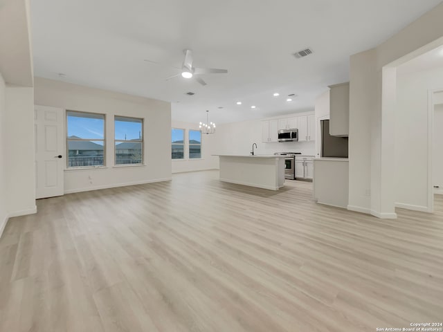 unfurnished living room with ceiling fan with notable chandelier, light wood-type flooring, and sink