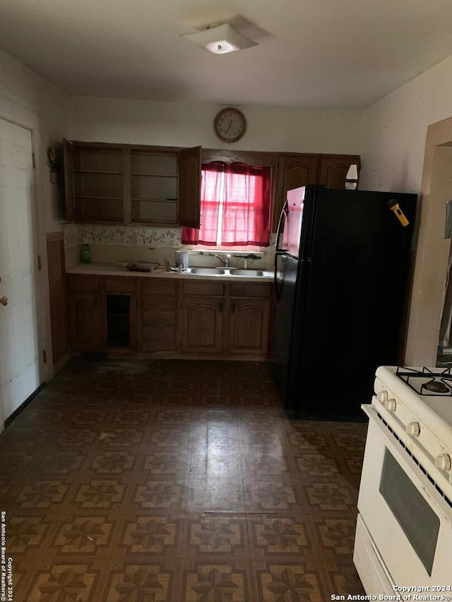 kitchen featuring white range with gas cooktop, black fridge, and sink