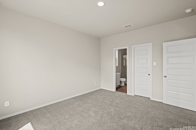 unfurnished bedroom featuring dark colored carpet and ensuite bathroom