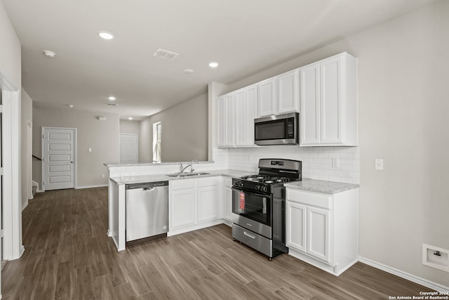 kitchen with white cabinets, appliances with stainless steel finishes, kitchen peninsula, and hardwood / wood-style floors