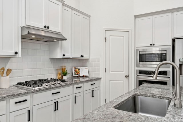 kitchen featuring decorative backsplash, light stone counters, stainless steel appliances, sink, and white cabinetry