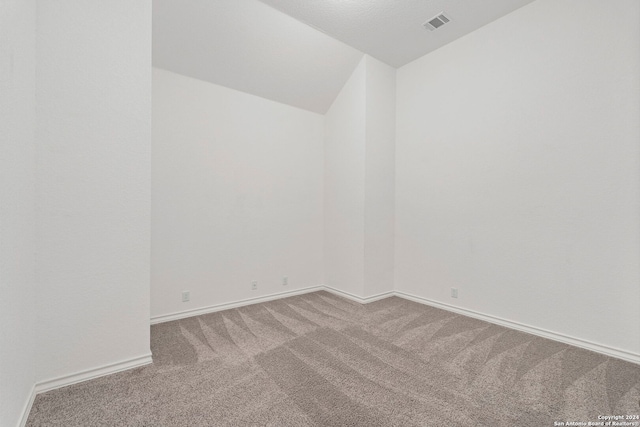 carpeted spare room with a textured ceiling and lofted ceiling