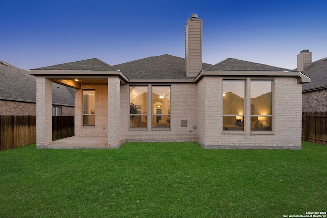 back house at dusk featuring a yard and a patio