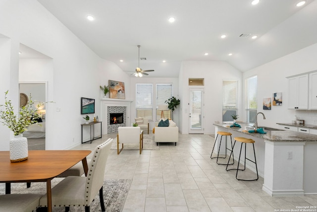 interior space with vaulted ceiling, ceiling fan, sink, light tile patterned floors, and a tiled fireplace