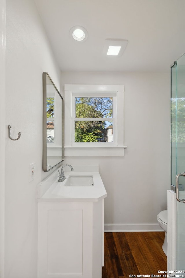 bathroom featuring wood-type flooring, toilet, a shower with shower door, and vanity