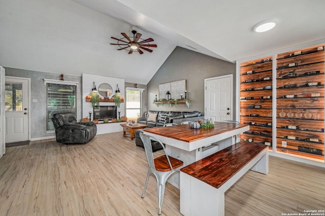 dining area featuring ceiling fan, a large fireplace, vaulted ceiling, and light wood-type flooring