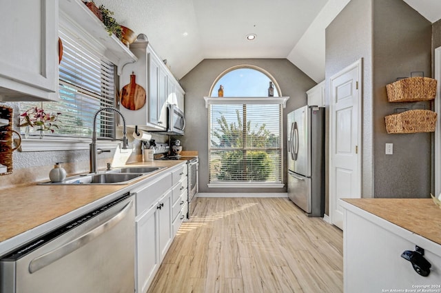 kitchen with lofted ceiling, white cabinets, sink, light hardwood / wood-style flooring, and appliances with stainless steel finishes