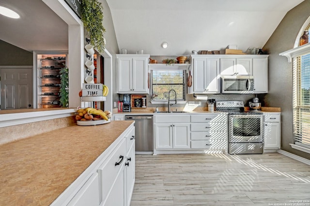 kitchen with stainless steel appliances, sink, light hardwood / wood-style flooring, white cabinets, and lofted ceiling