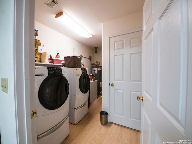 laundry area with washing machine and dryer, electric water heater, and light hardwood / wood-style floors