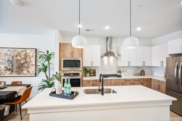 kitchen with decorative light fixtures, stainless steel appliances, wall chimney exhaust hood, and sink