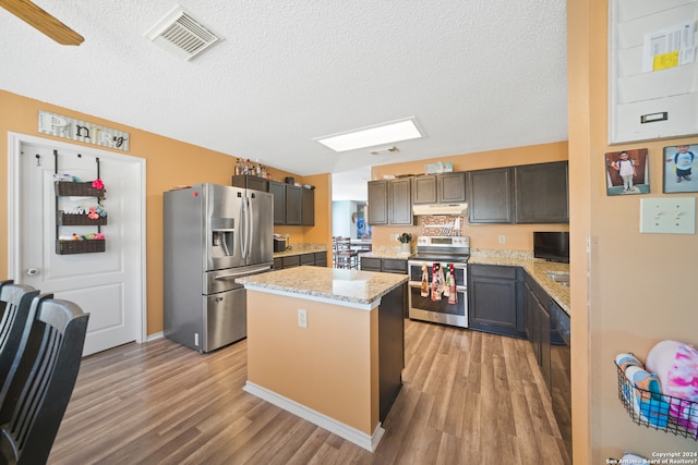 kitchen with light wood-type flooring, a textured ceiling, stainless steel appliances, dark brown cabinetry, and a kitchen island