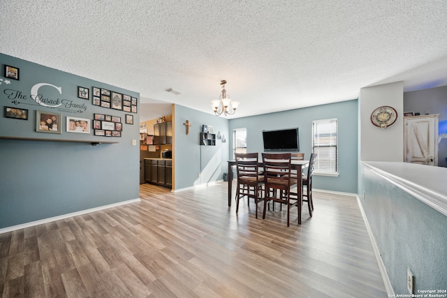 dining room featuring a textured ceiling, light wood-type flooring, and a notable chandelier