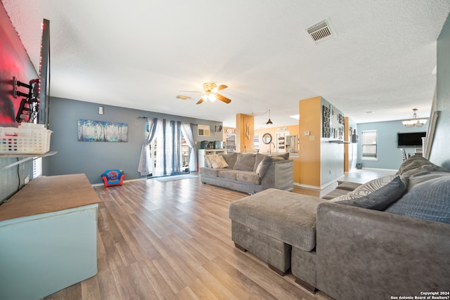 living room featuring ceiling fan with notable chandelier, a textured ceiling, and light hardwood / wood-style flooring