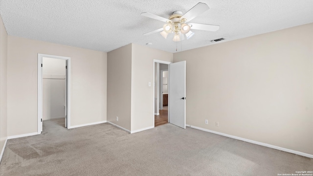 unfurnished bedroom with ceiling fan, light colored carpet, a textured ceiling, a walk in closet, and a closet