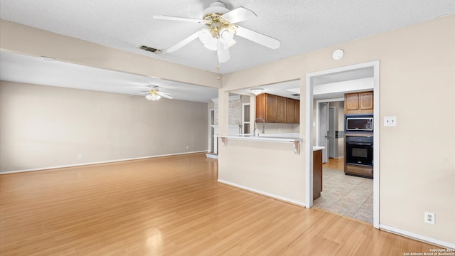 interior space featuring black appliances, a kitchen breakfast bar, a textured ceiling, light hardwood / wood-style floors, and kitchen peninsula