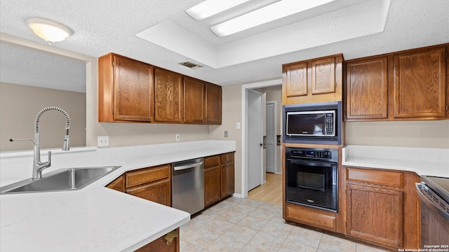 kitchen with sink, light tile patterned floors, black appliances, and a textured ceiling