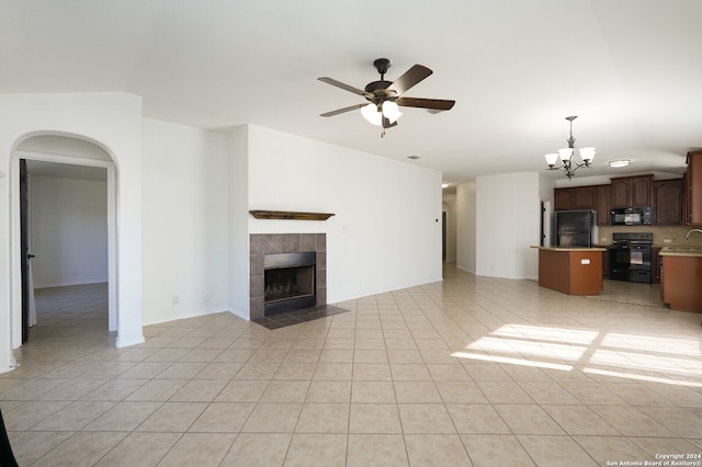 unfurnished living room with a tiled fireplace, light tile patterned floors, and ceiling fan with notable chandelier