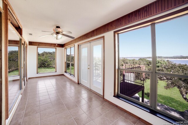 unfurnished sunroom featuring ceiling fan, french doors, and a water view