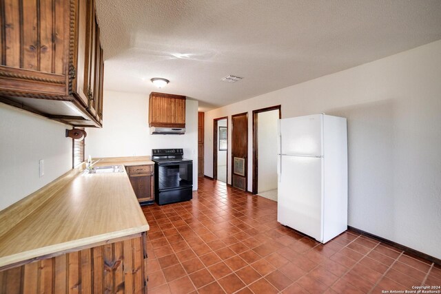 kitchen with a textured ceiling, sink, white refrigerator, black electric range oven, and range hood