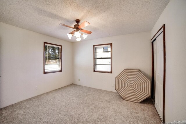 unfurnished bedroom with a textured ceiling, ceiling fan, light carpet, and multiple windows