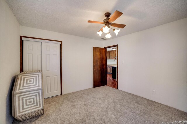 unfurnished bedroom with carpet, a textured ceiling, a closet, and ceiling fan