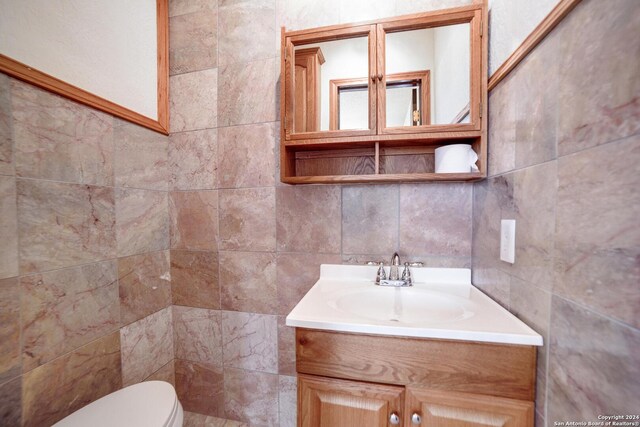 bathroom with vanity, toilet, and tile walls