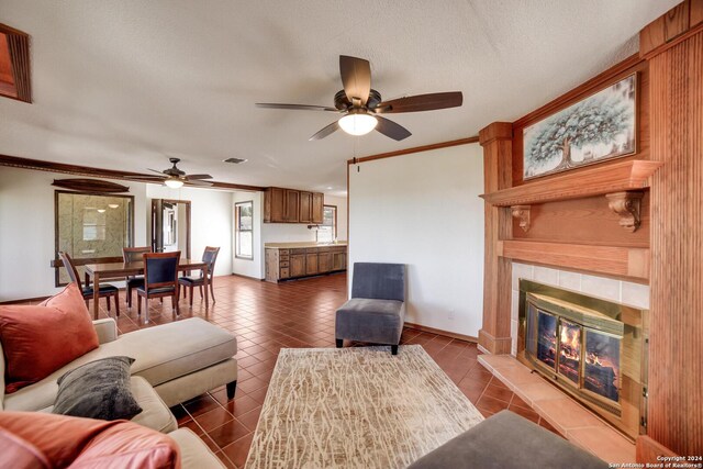 living room with tile patterned flooring, ceiling fan, ornamental molding, and a tile fireplace