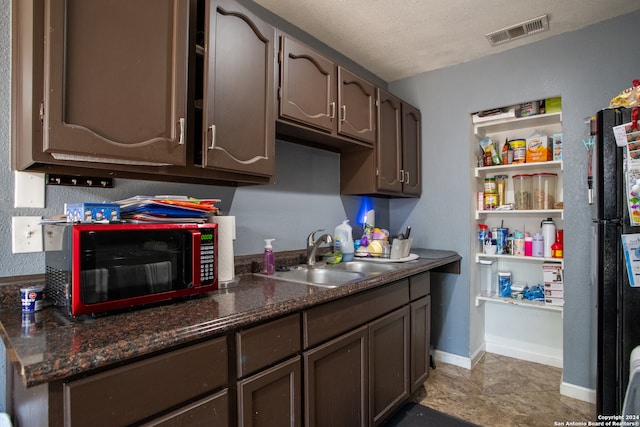 kitchen with a textured ceiling, refrigerator, dark brown cabinets, and sink