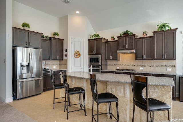 kitchen with stainless steel appliances, tasteful backsplash, light stone counters, a kitchen island with sink, and a breakfast bar