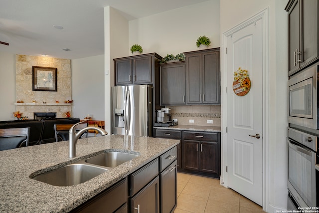 kitchen featuring sink, light tile patterned floors, dark brown cabinets, light stone counters, and stainless steel appliances