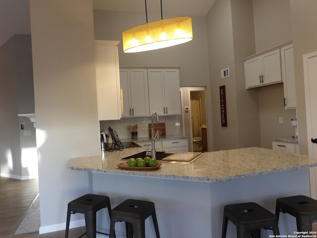 kitchen with kitchen peninsula, pendant lighting, wood-type flooring, a breakfast bar, and white cabinets