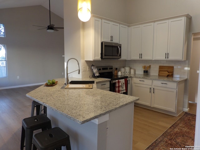 kitchen with kitchen peninsula, sink, electric range, white cabinets, and a breakfast bar area