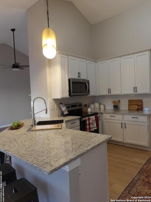 kitchen with kitchen peninsula, appliances with stainless steel finishes, sink, high vaulted ceiling, and white cabinets