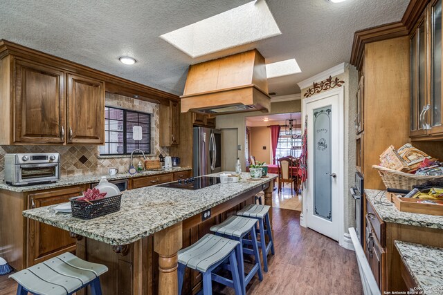 kitchen with dark hardwood / wood-style flooring, a breakfast bar, black electric cooktop, a center island, and stainless steel refrigerator