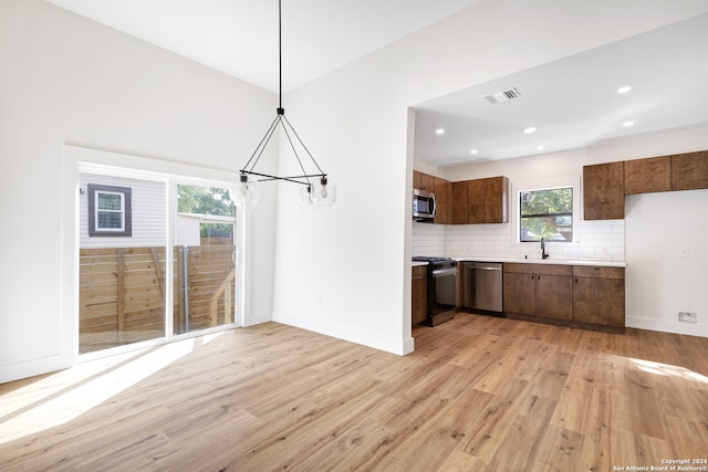 kitchen with sink, backsplash, light hardwood / wood-style floors, pendant lighting, and appliances with stainless steel finishes