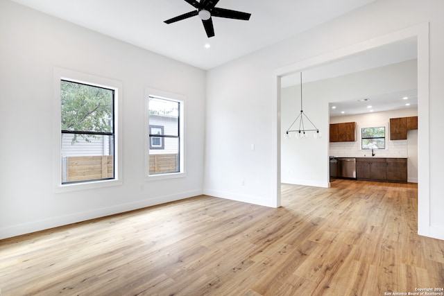 empty room with ceiling fan with notable chandelier, a healthy amount of sunlight, and light hardwood / wood-style flooring