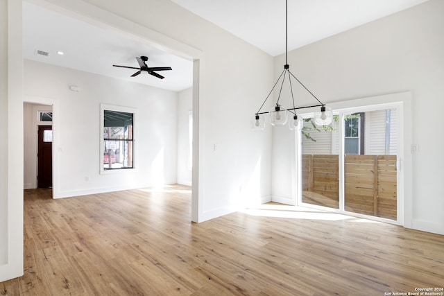 unfurnished dining area with ceiling fan with notable chandelier and light wood-type flooring